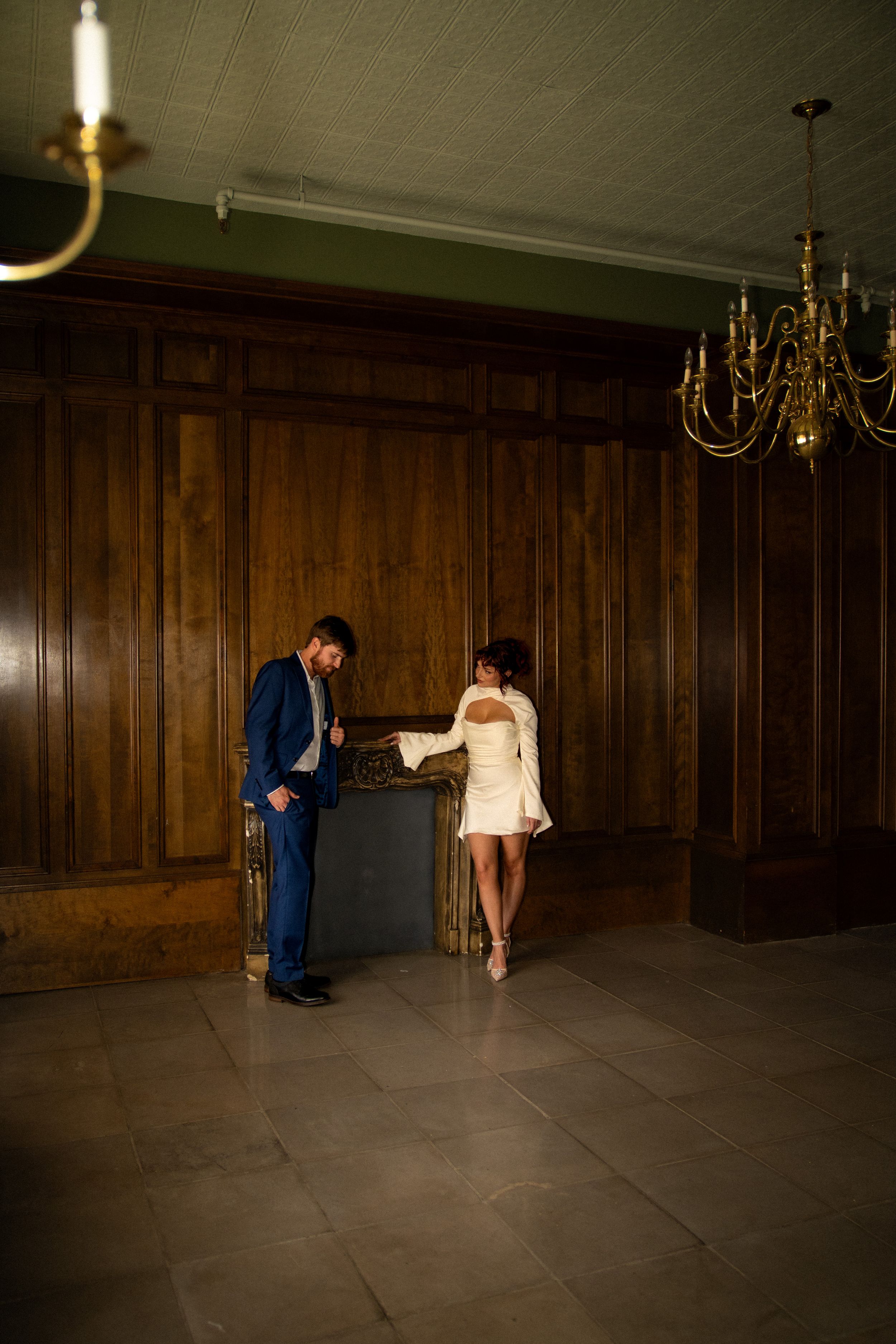 Artistic wedding photo in wood-paneled room with dramatic lighting and chandelier.