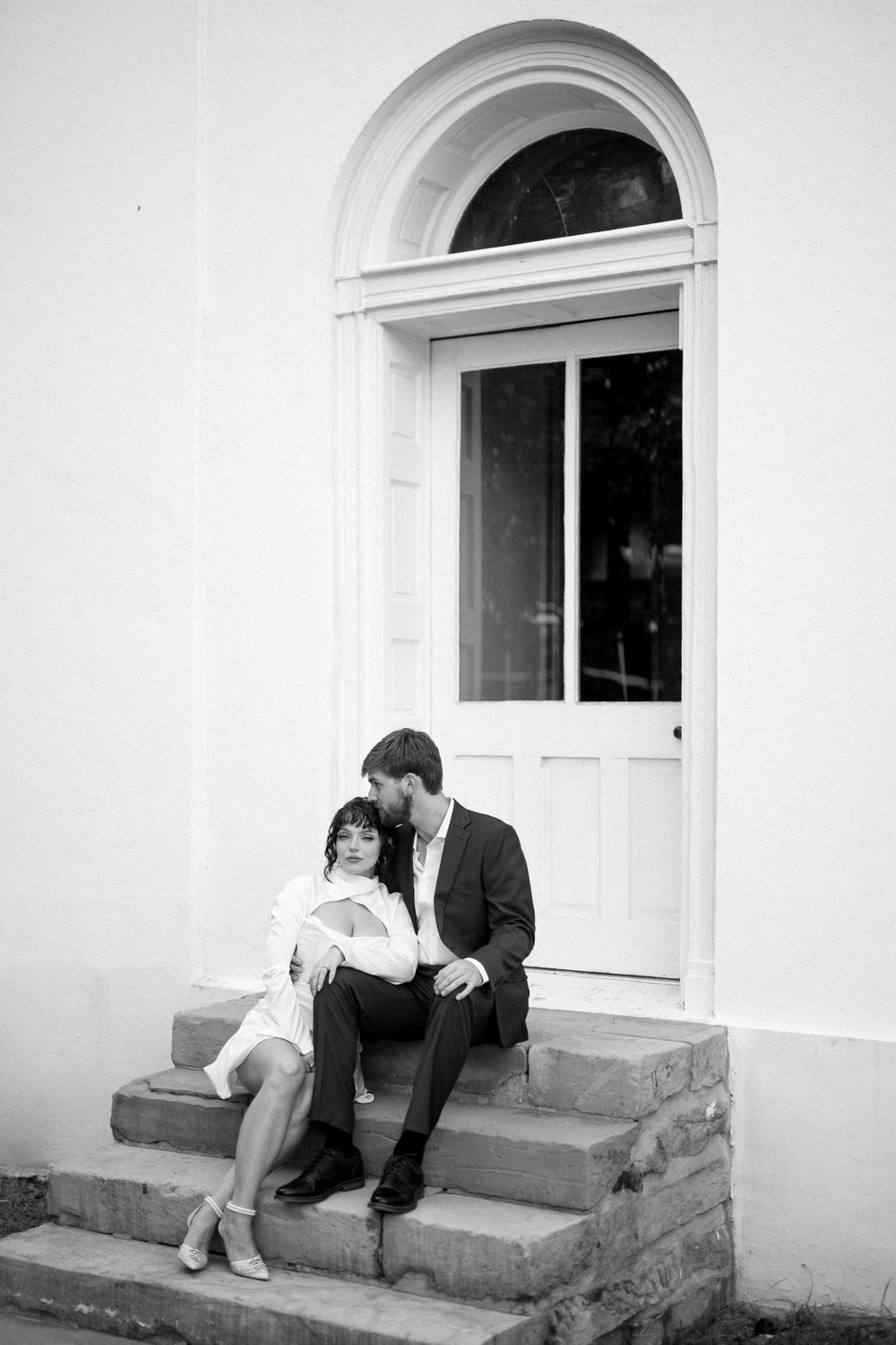 Black and white photo of a couple sharing a tender moment on stone steps.