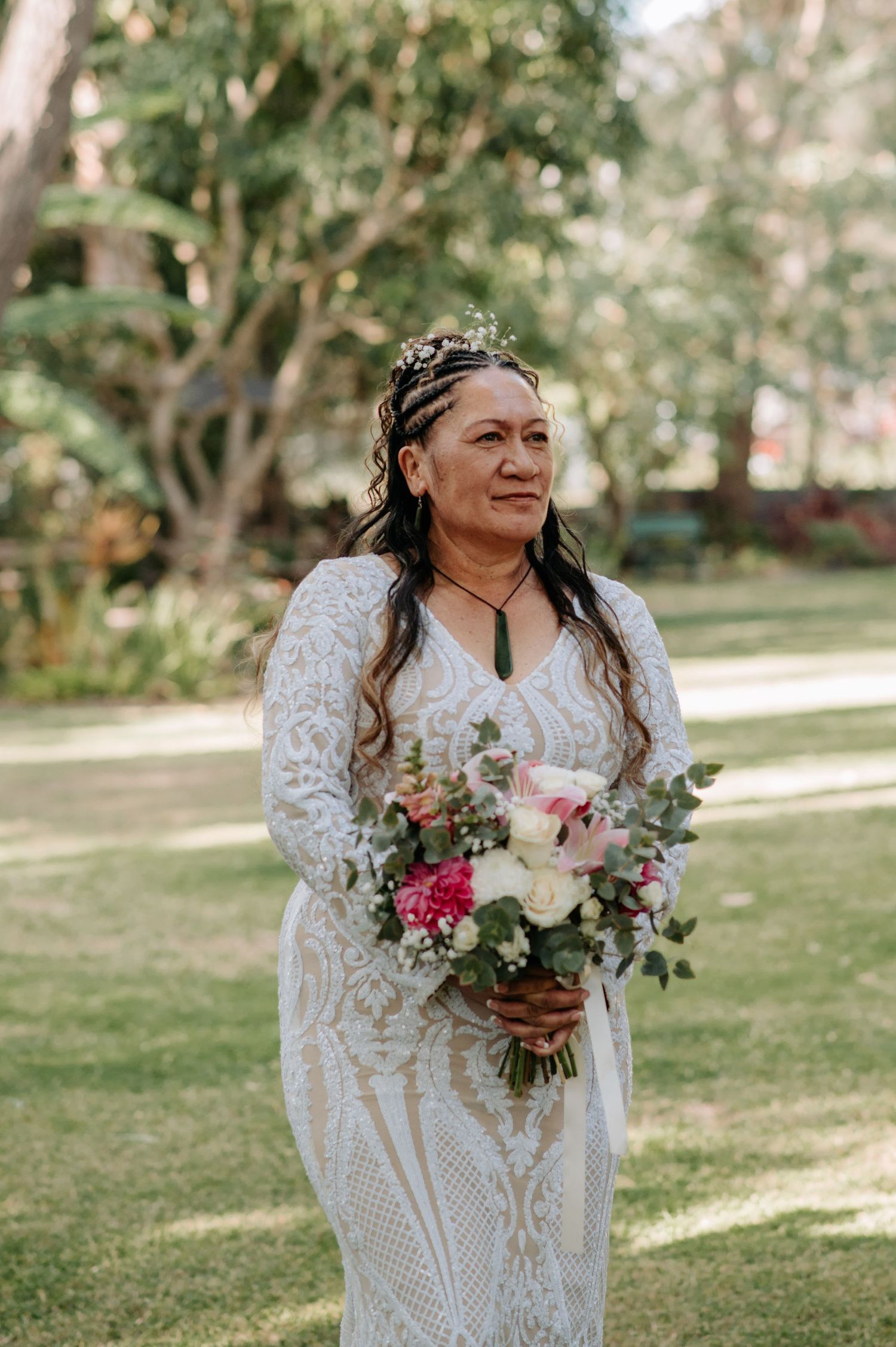 Bride in detailed lace gown holds colorful bouquet in garden setting.