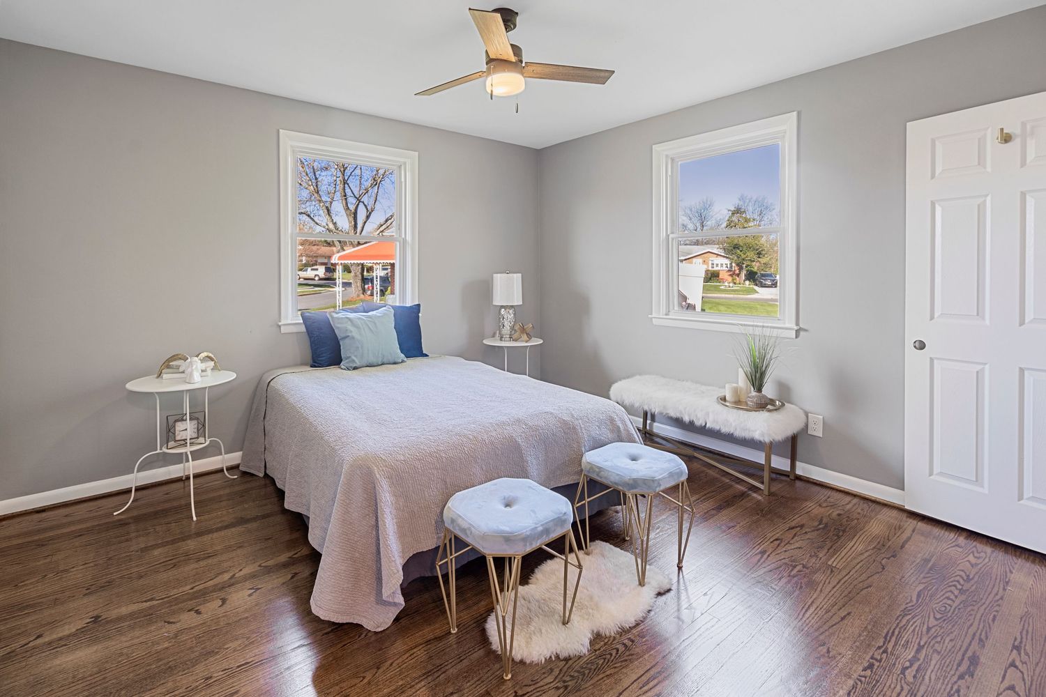 Modern bedroom with gray walls, hardwood floors, and round metallic accent tables.