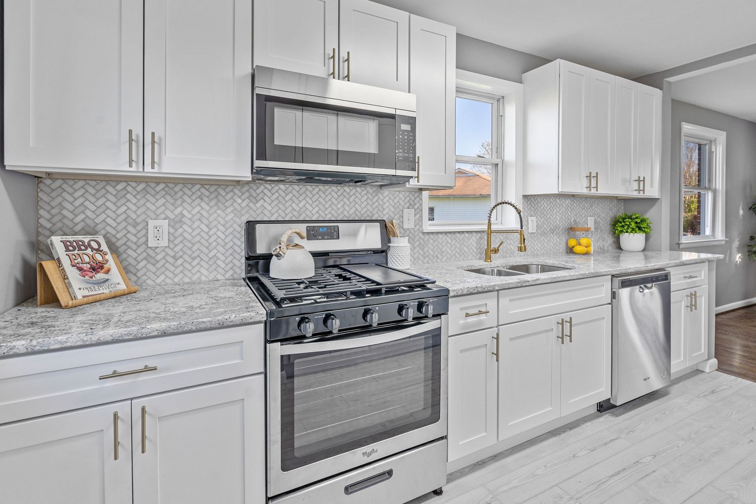White kitchen with marble countertops, subway tile backsplash, and stainless steel appliances.