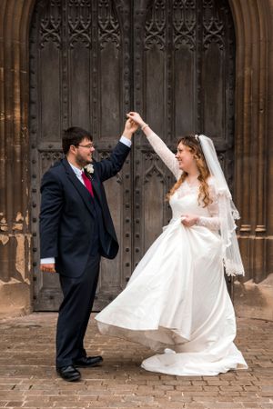 A playful wedding couple dances and twirls in front of ornate gothic doors.