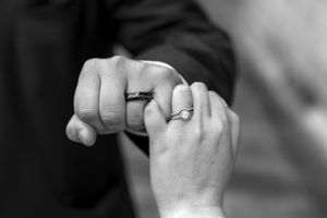 Close-up of wedding rings and clasped hands in black and white.