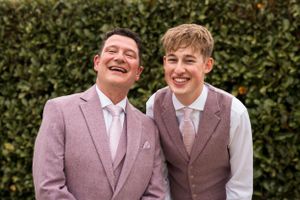 Wedding party members in mauve suits sharing a laugh outdoors.