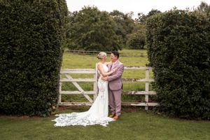 Wedding couple posing together in garden setting with white fence and hedges.