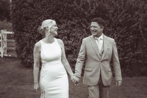 Wedding couple walking hand in hand through garden setting in black and white.