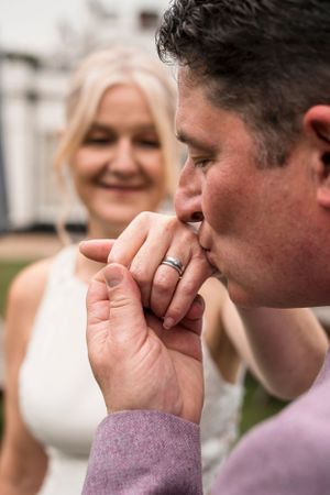 A tender moment captured during a wedding ceremony as a ring is kissed while wearing formal attire.