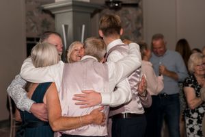 Wedding guests embrace in a group hug during an emotional reception moment.