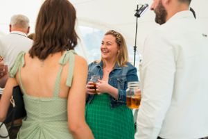 Wedding reception guests mingle and socialize in a white tent with green accents.