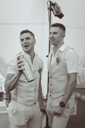 Groomsmen in white and beige attire share laughs during wedding celebration.