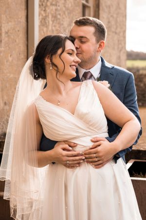 A tender embrace between newlyweds in front of a stone building.