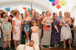 Wedding guests dance and celebrate under a tent decorated with colorful balloons.