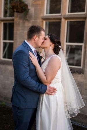 A romantic wedding kiss against rustic stone architecture.