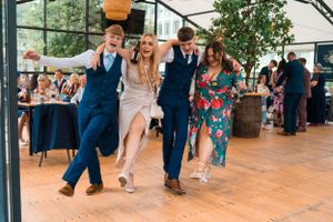 Wedding guests dancing energetically on a wooden dance floor at an indoor reception.