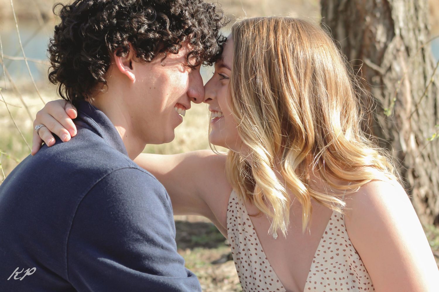 A couple shares a tender moment outdoors in front of a rustic wooden background.