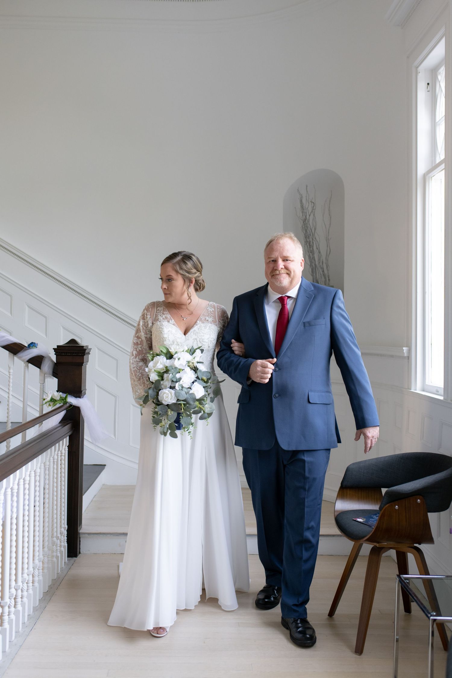 A traditional white wedding staircase with elegant dark wood banister and decorative wainscoting.