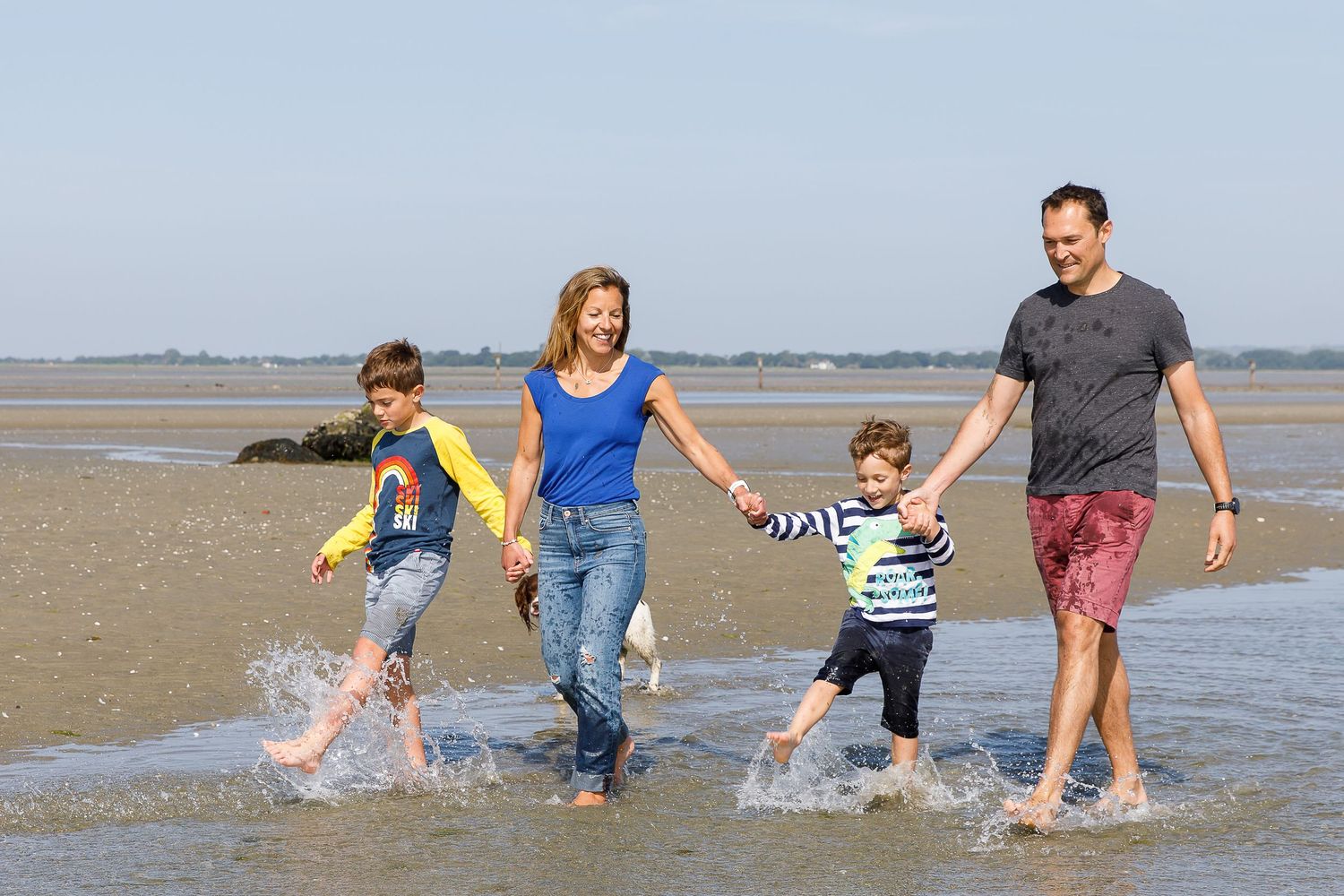 A family splashes together in shallow beach water on a sunny day during a family beach photoshoot