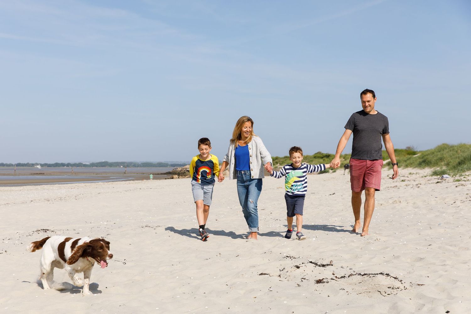 A family takes a beach walk together with their spotted dog leading the way during a family beach photoshoot