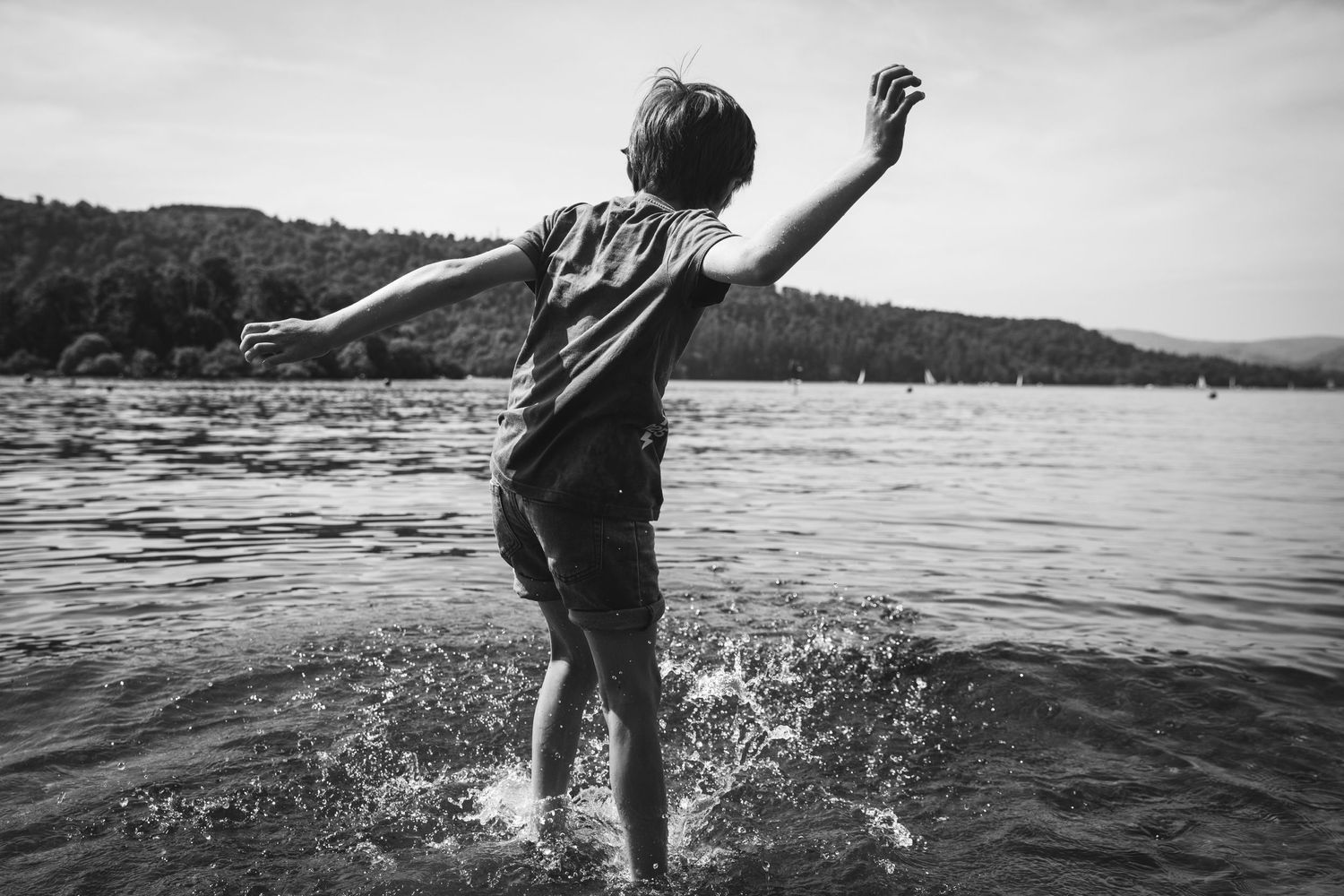 Silhouette of person jumping and splashing in a lake with mountains in the background.