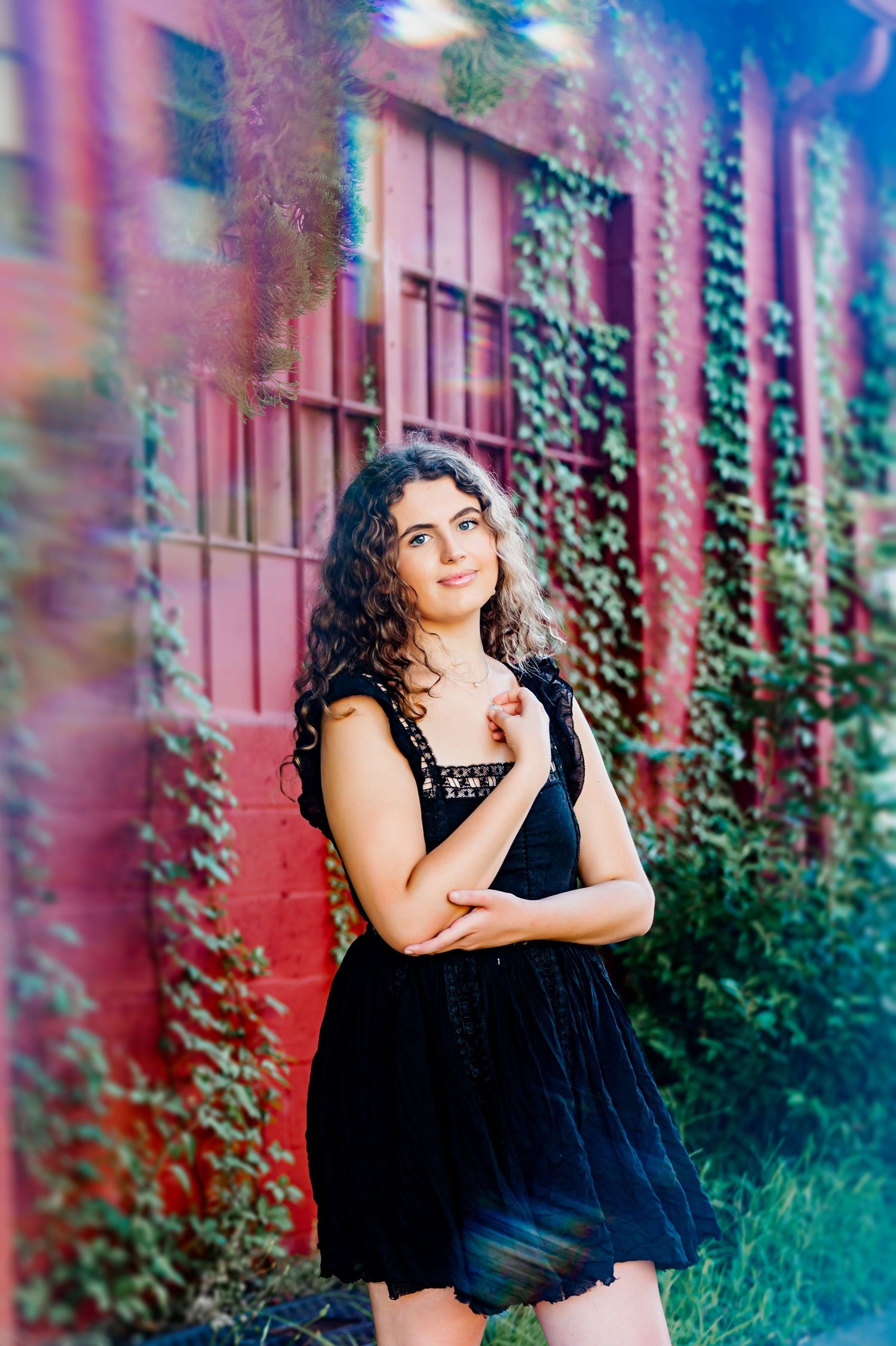 A fashion portrait against a red wall with climbing vines featuring a black dress.
