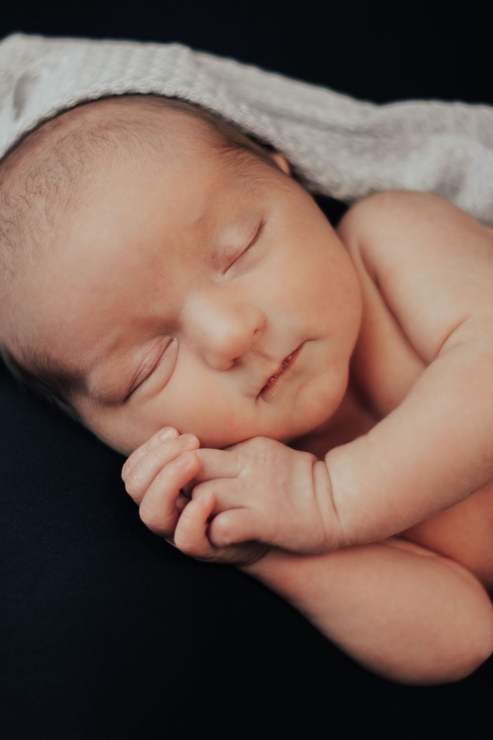 Peaceful newborn sleeping on white blanket against black background in classic portrait style.
