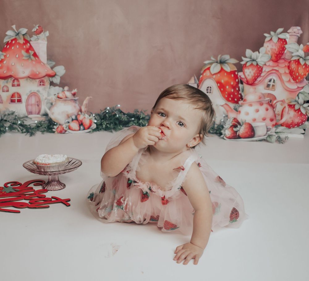 Baby in pink dress reaching towards dessert with decorative mushroom houses in background.