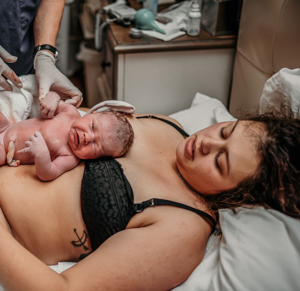mom lying on the bed, with just birthed baby lying on her chest, face up, looking right at the camera