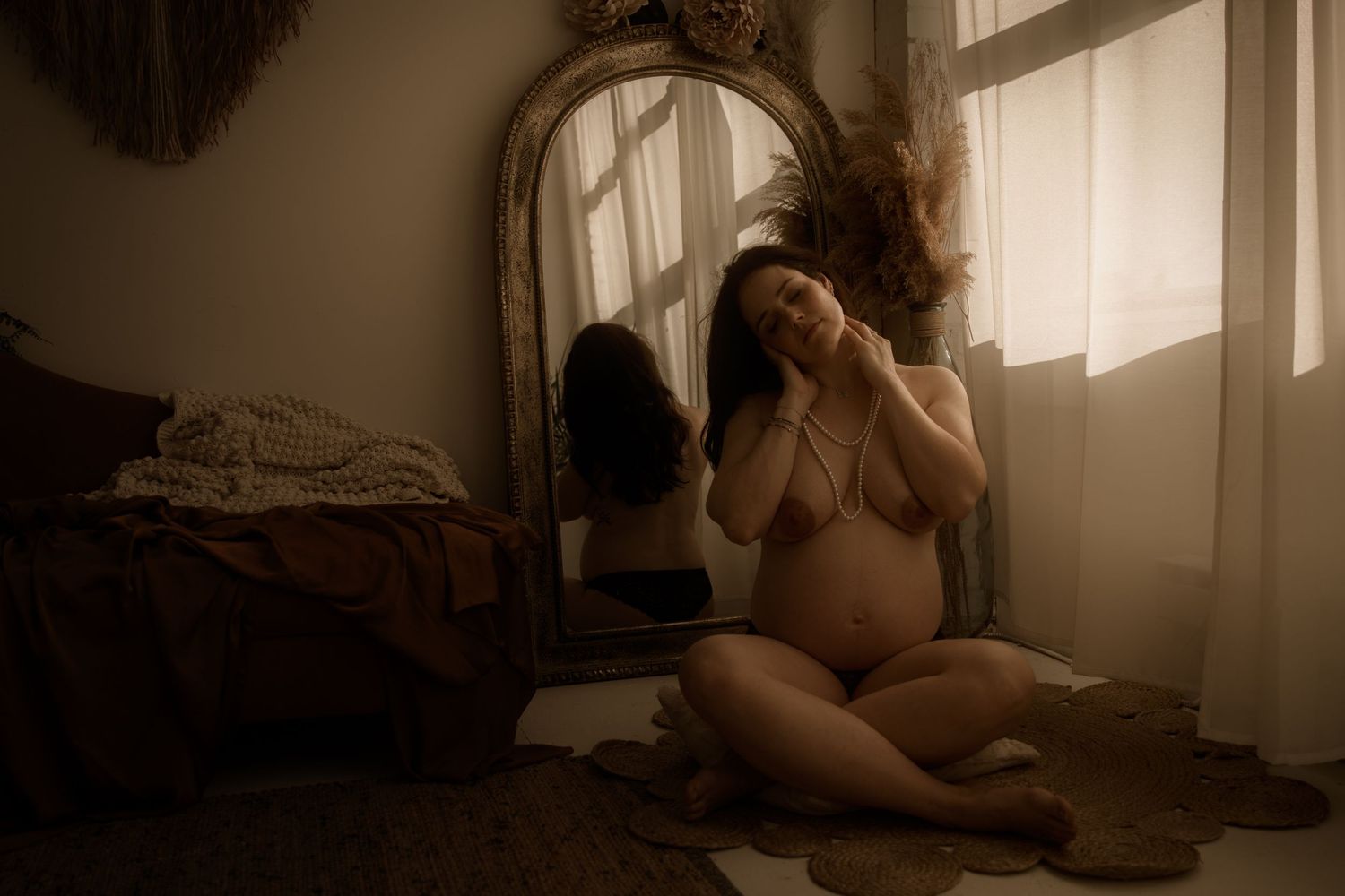 A silhouette in lingerie poses near a window with a mirror in a moody, sepia-tinted boudoir setting.