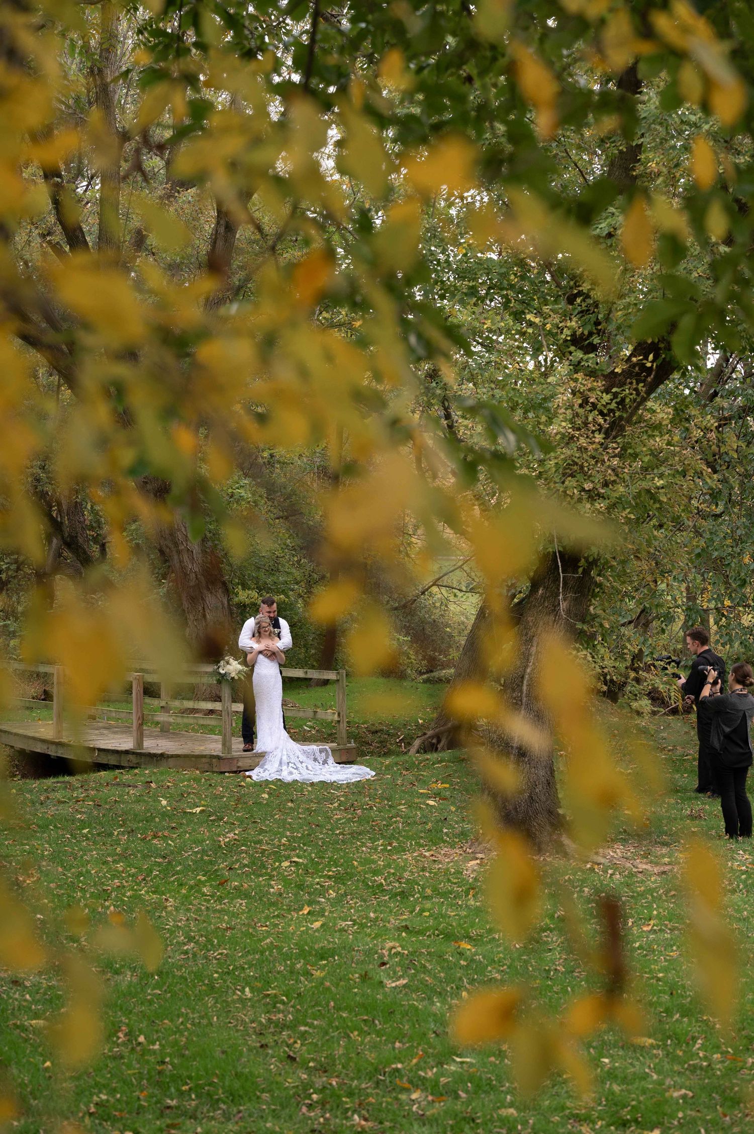A wedding dress figure framed by golden autumn leaves in a serene outdoor setting.