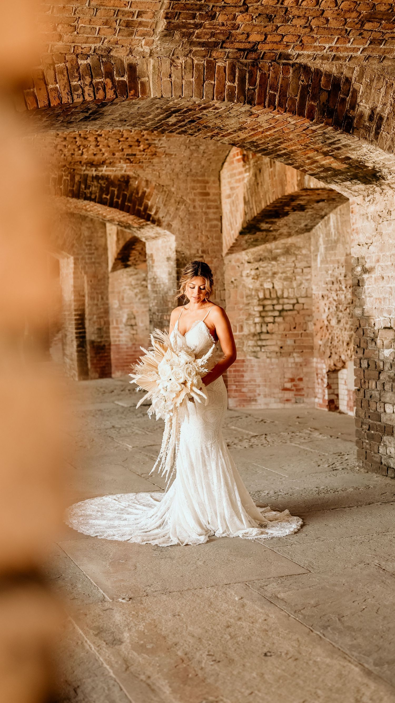 Elegant bridal portrait with dried palm bouquet in historic brick archway.