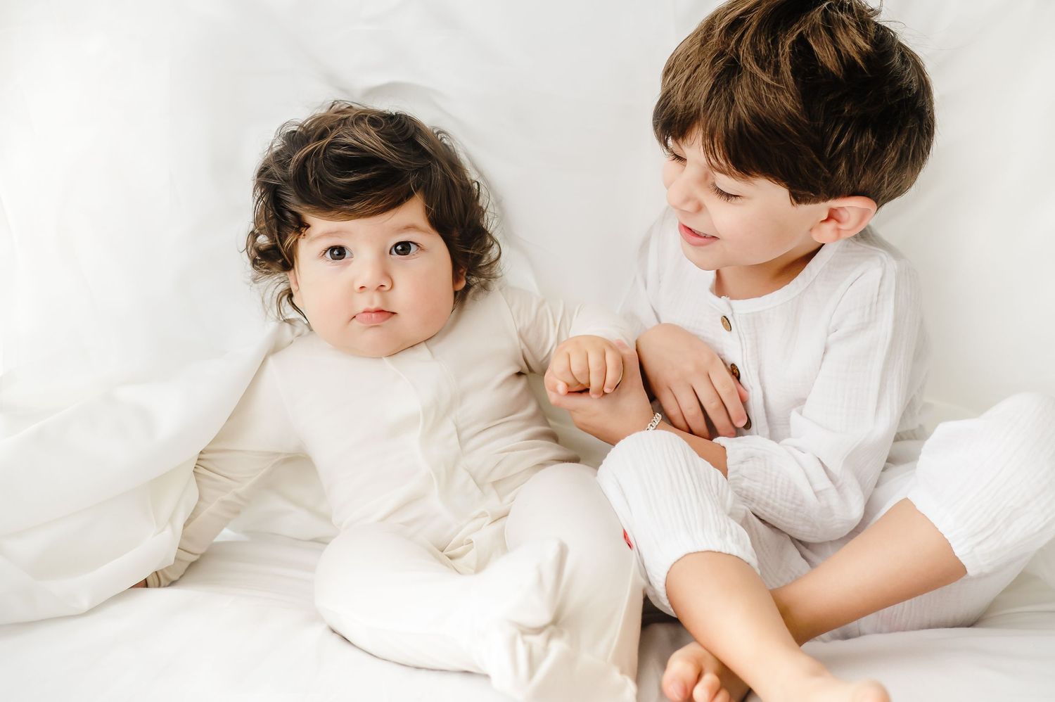 siblings wearing all white playing in the sheets during a in home lifestyle session