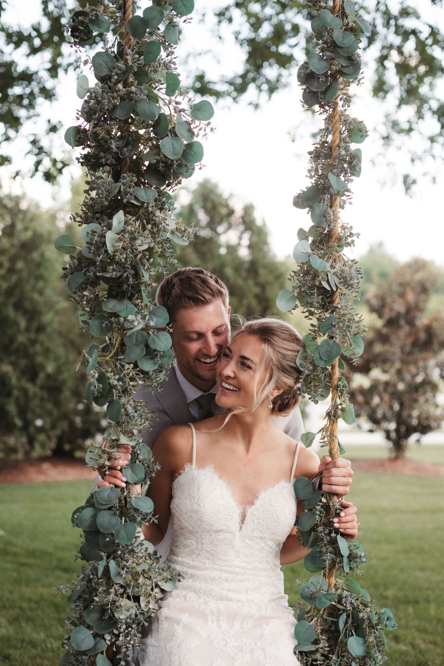 A couple shares a romantic moment on a floral-decorated swing in an outdoor garden setting.