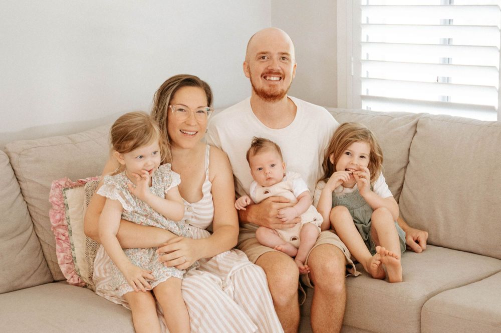Casual family portrait on a beige couch in a bright, airy room.