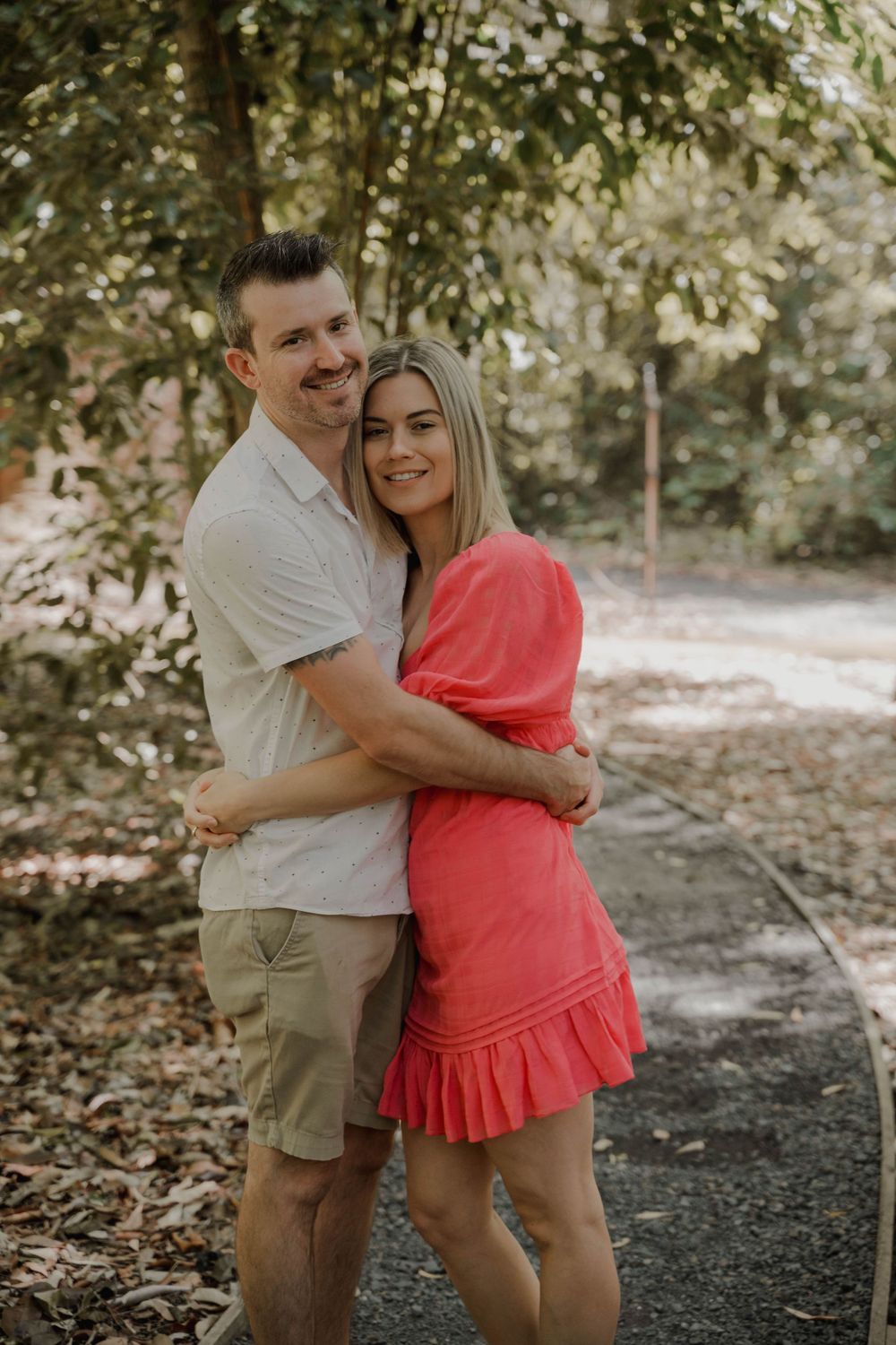 A couple embraces outdoors wearing coordinating beige and coral outfits.