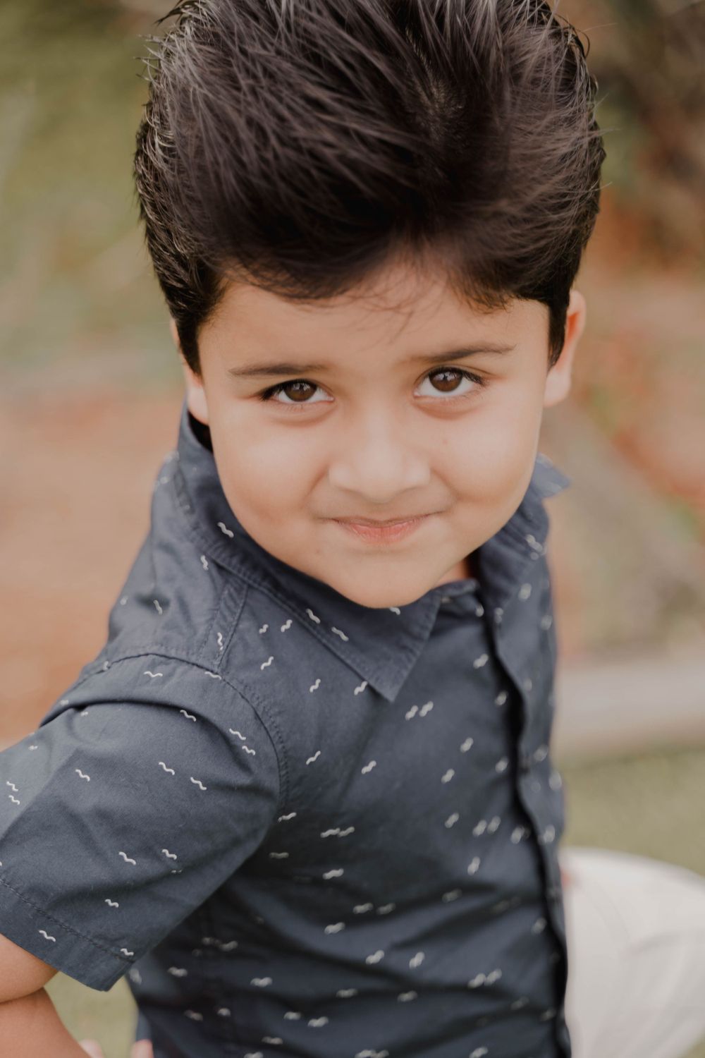 Close up portrait of a child in a navy patterned shirt smiling at the camera.