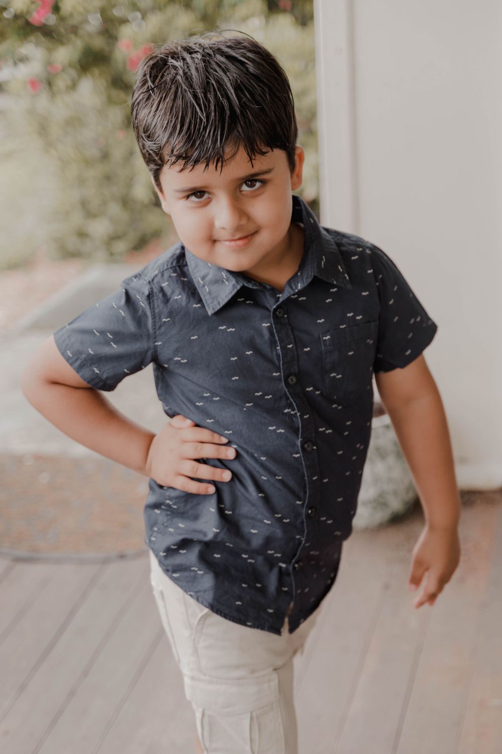 A young boy in a gray patterned shirt poses with hand on hip.