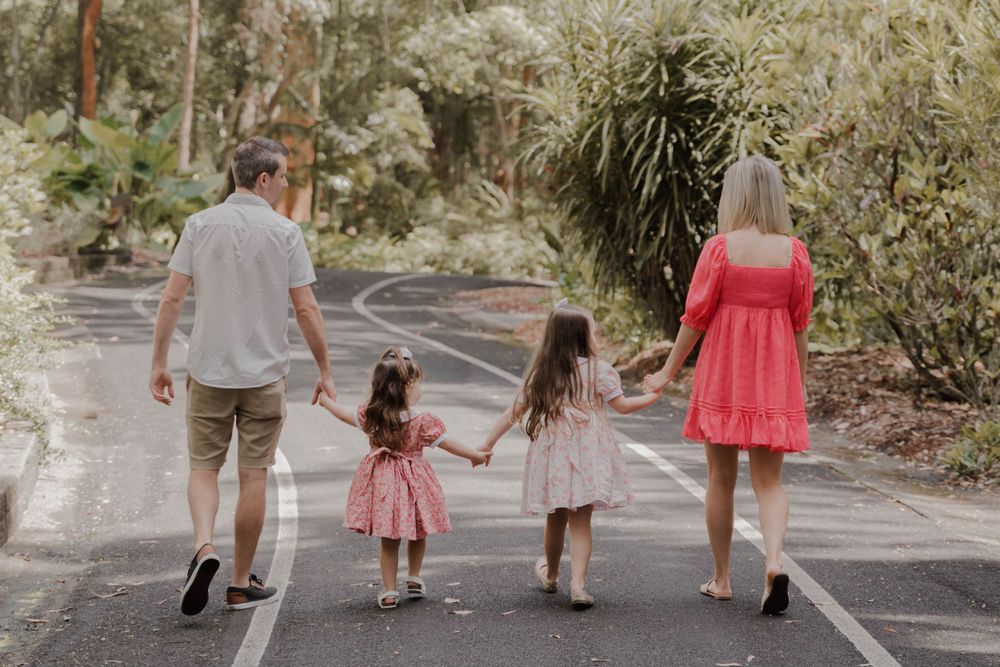 A family walks together down a tree-lined path holding hands.
