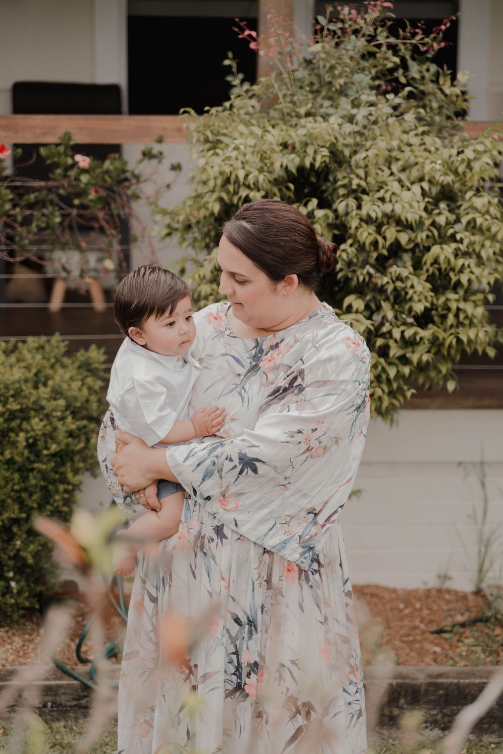 A tender outdoor portrait showing a mother in a floral dress embracing a small child.