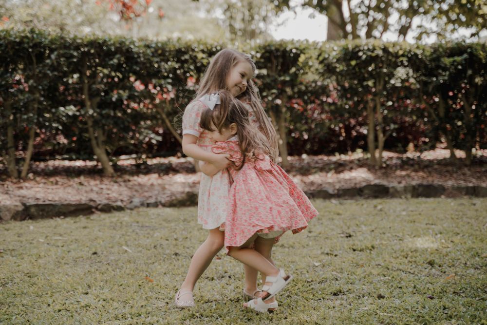 A child in a pink dress twirls playfully on grass with greenery in the background.