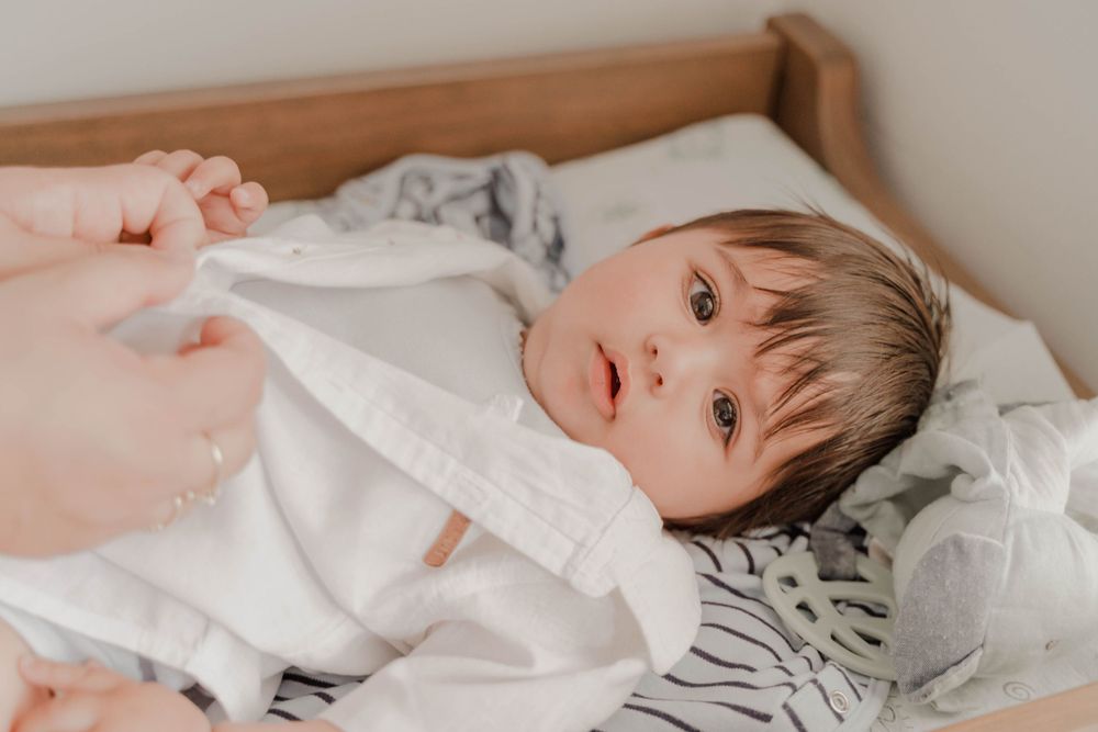 A baby lies in white bedding looking up at the camera.