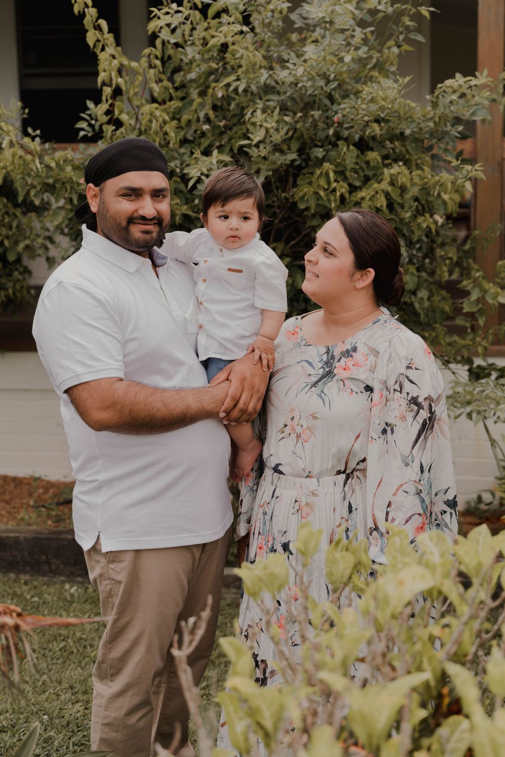 Family portrait in a garden setting with parents and young child against greenery.