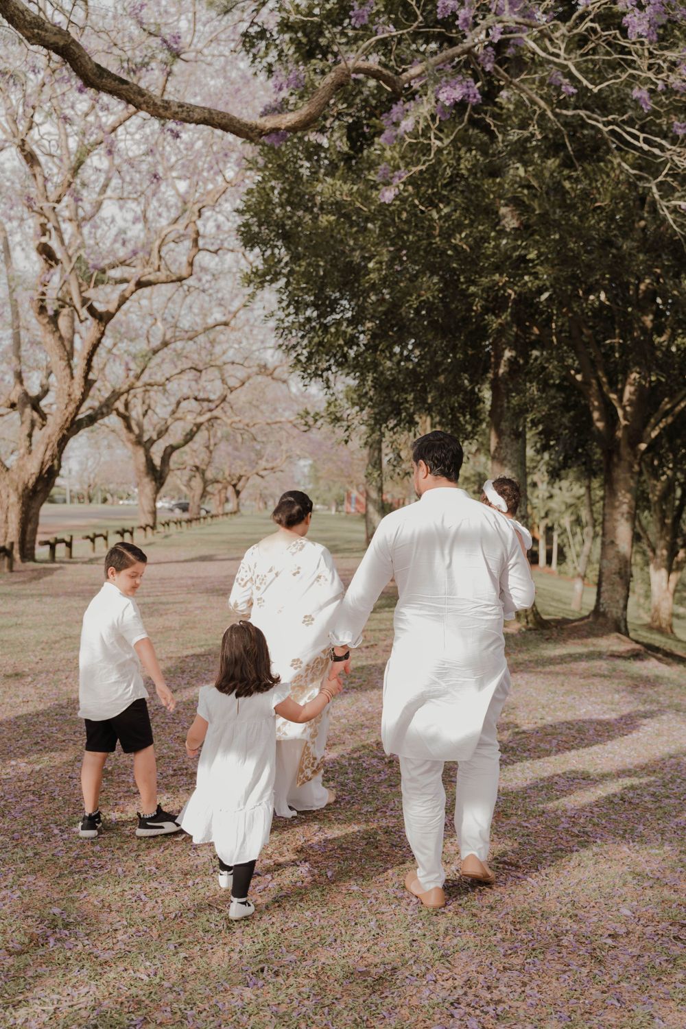 Family walking together down a tree-lined path in matching white outfits.