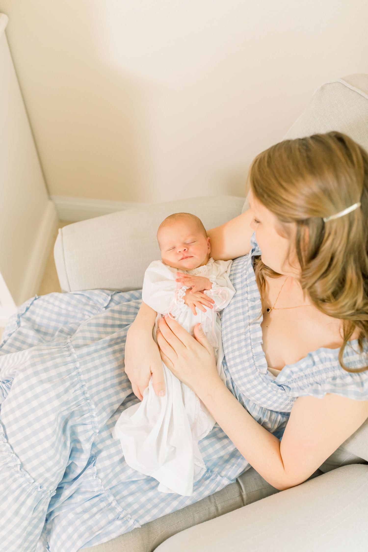 Tender moment between parent and newborn on gray chair in nursery.