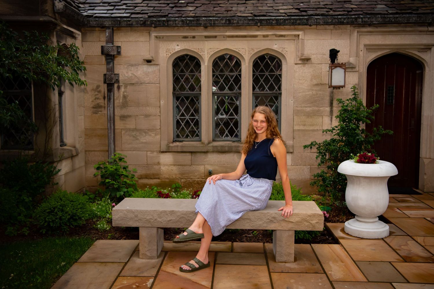 high school senior girl in navy shirt sitting in front of large windows