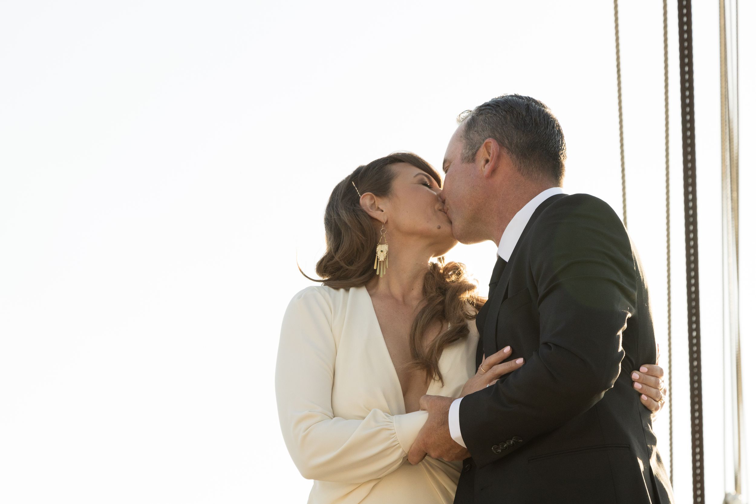 A romantic wedding kiss between a couple in formal attire by a window. Shot By Zeus Holbrook San Diego Wedding Photographer