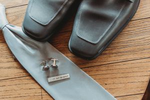 Silver cufflinks and dress shoes arranged on wooden floor for wedding day preparation.