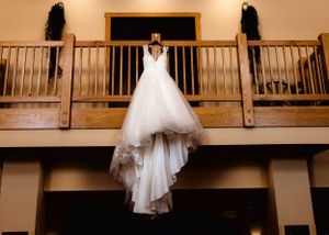 A white wedding dress hangs elegantly from a wooden balcony railing.