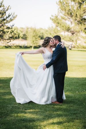 A couple embraces on a sunny lawn as the bride's white wedding dress flows gracefully in the breeze.