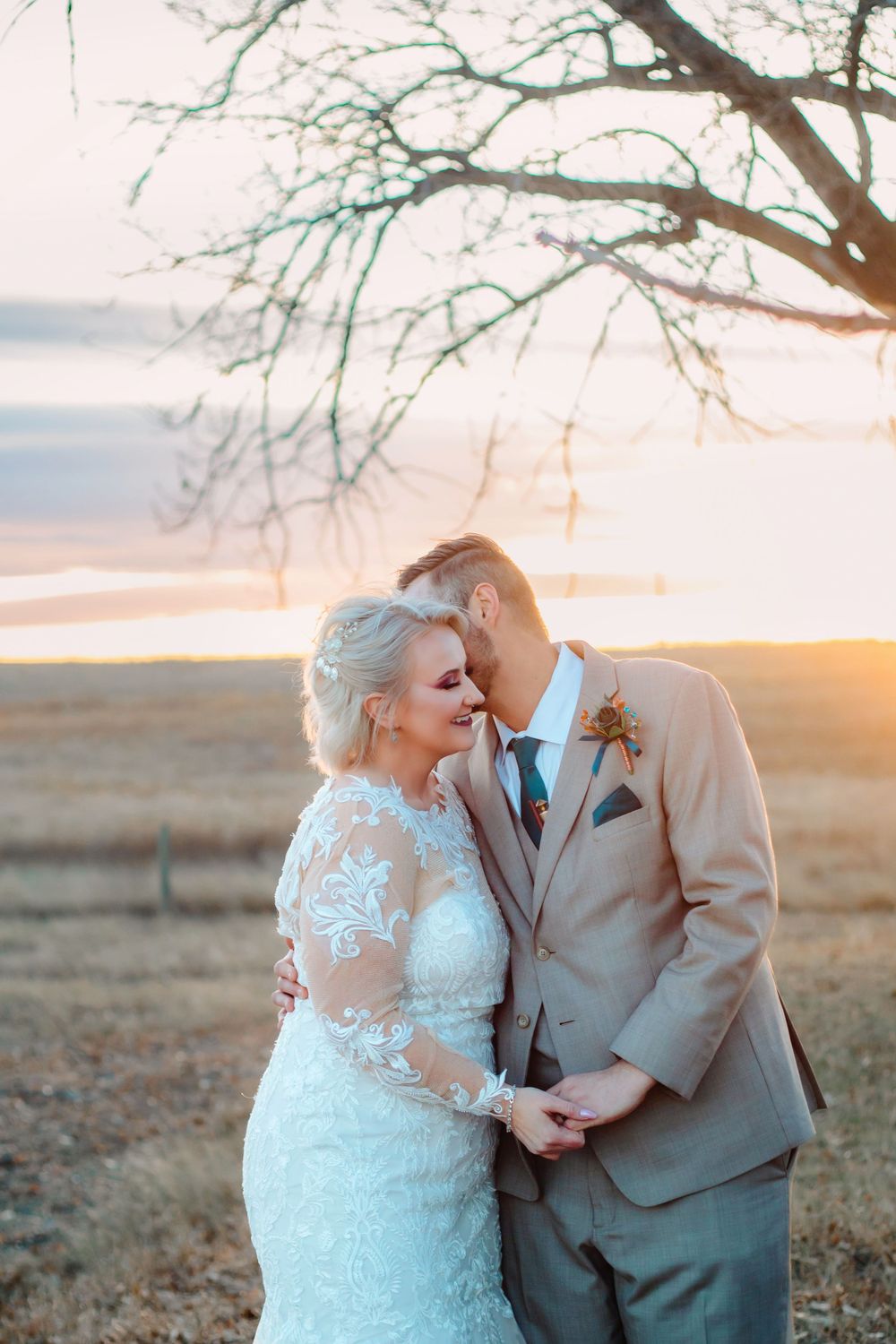 A romantic golden sunset moment at a countryside wedding with a couple embracing in formal attire.