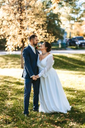 A romantic wedding couple embraces outdoors on an autumn day with golden sunlight and fall foliage in the background.